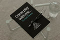 Black notebook with 'Come play with me... I've Got Games' text and a pen on a glass table.