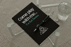 Black notebook with 'Come play with me... I've Got Games' text and a pen on a glass table.